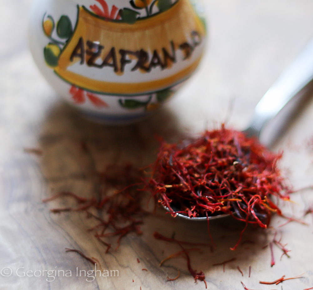 teaspoon of vibrant red saffron fronds on wooden board